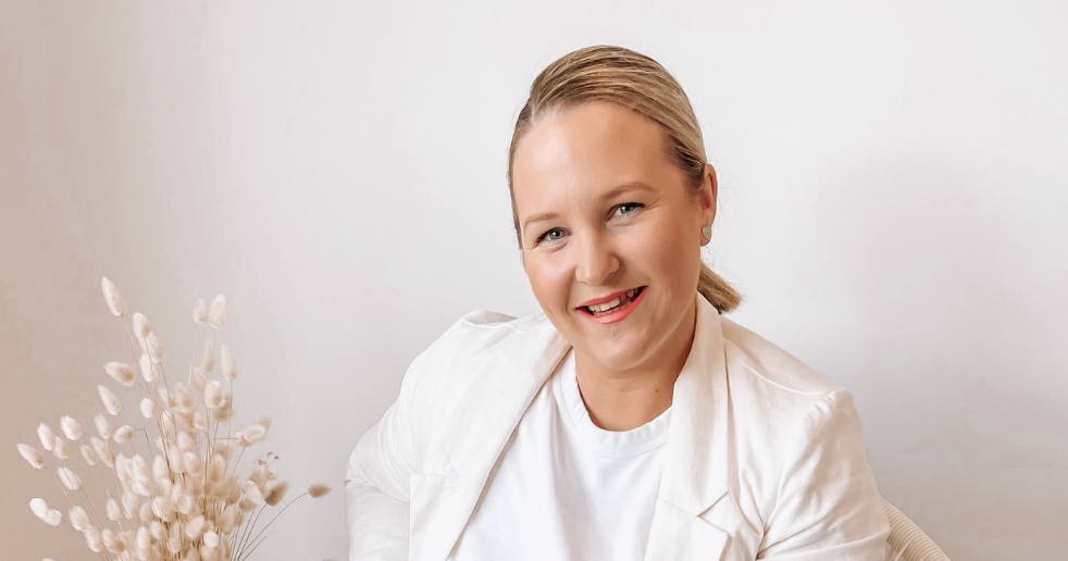 Hayley Murray smiling in a soft white blazer, pampas grass beside her.