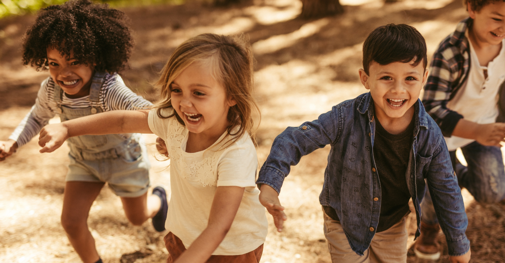 Three children running through a sunlit field, laughing.